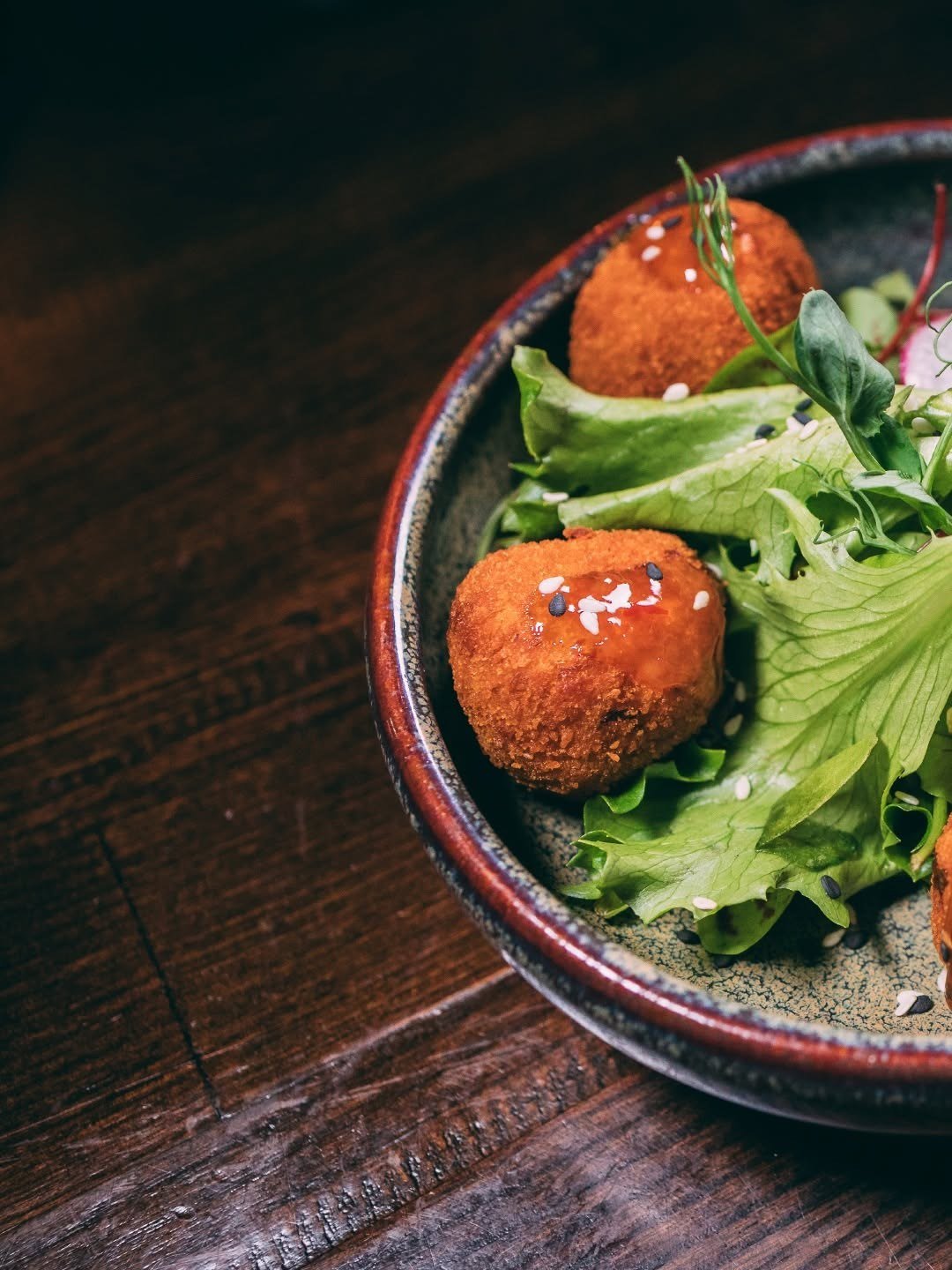 Croquetes dourados sobre salada verde numa taça escura